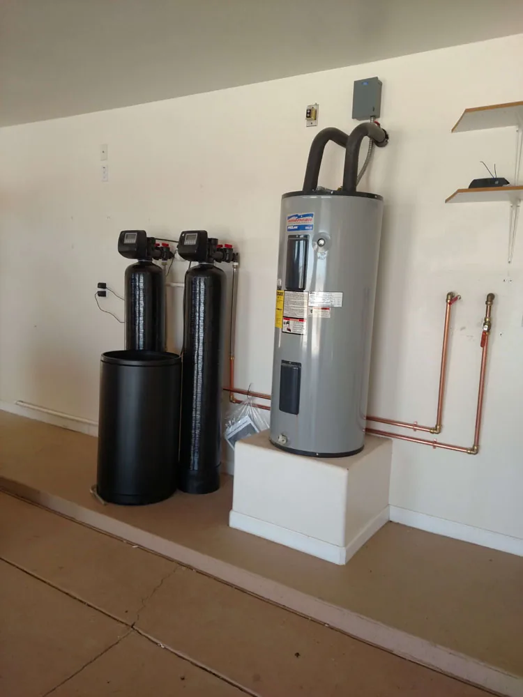 Water softener and filtration tanks installed beside a water heater in a garage