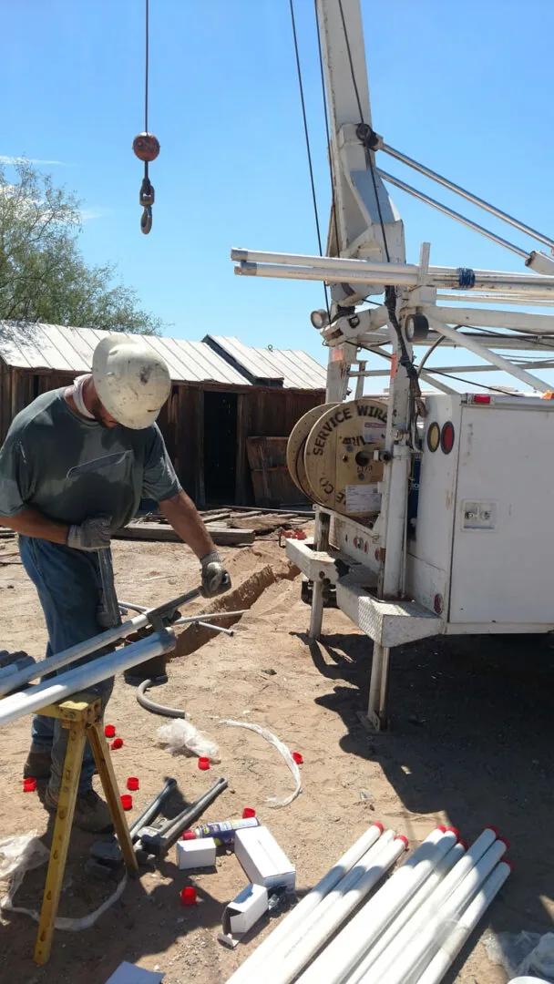 An Affordable Pump Service technician cutting pipe beside the pump hoist truck, with a reel of well wire and lengths of drop pipe on the ground